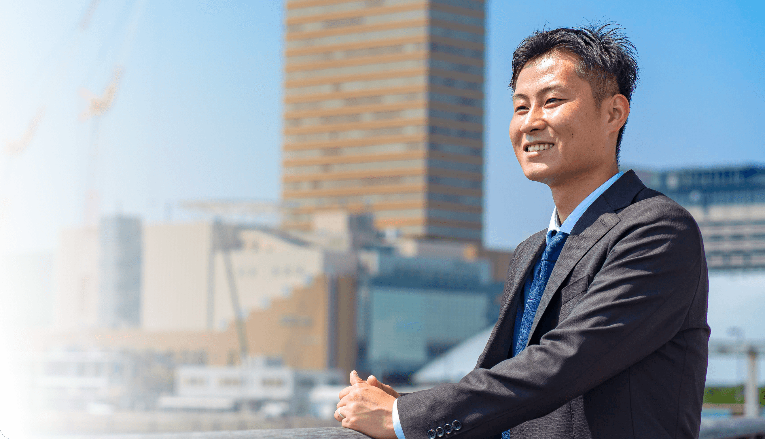 学生服で笑顔の若い男性が外でもたれかかっている様子